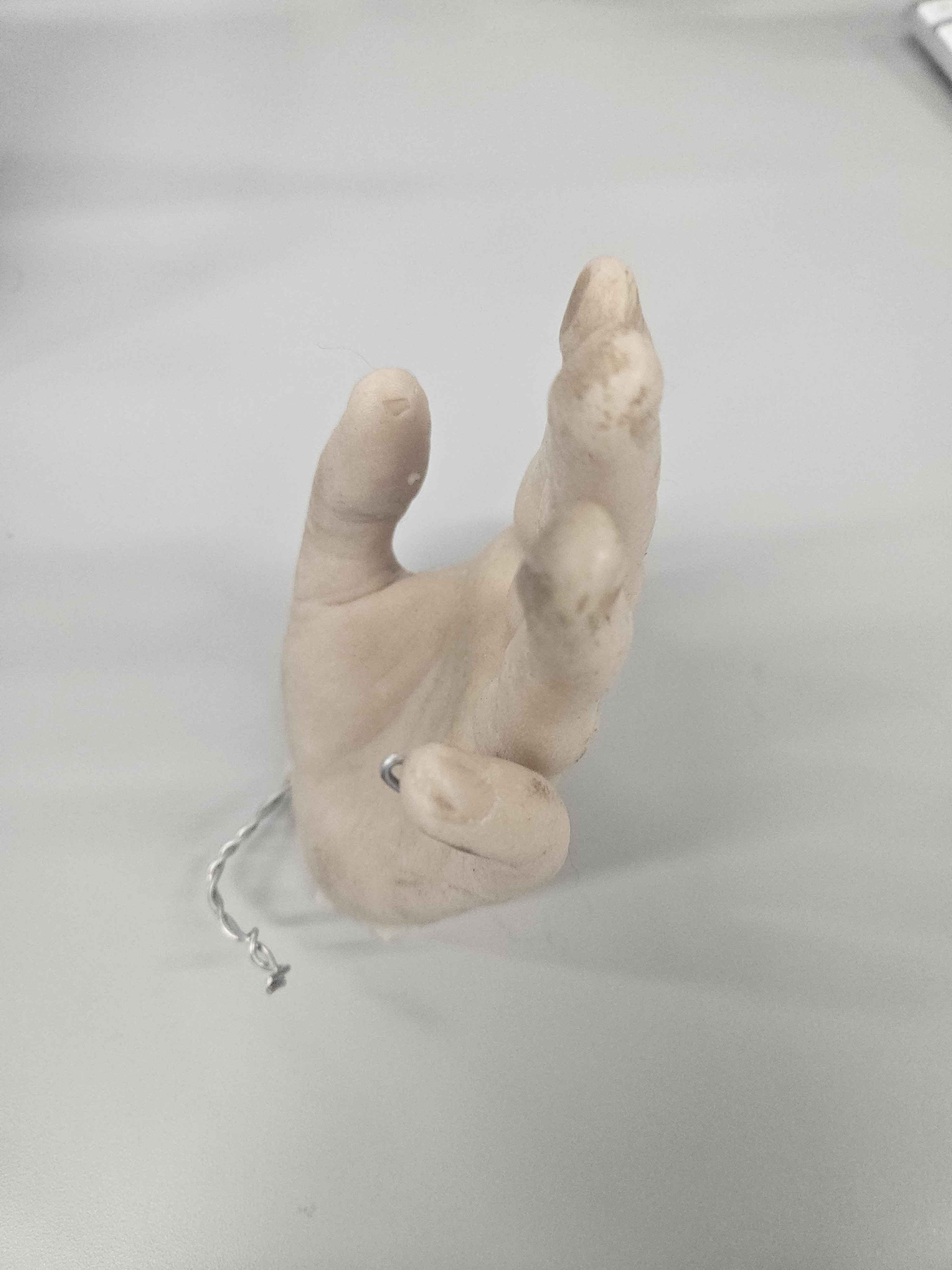 This is a plastic polymer material shaped as a hand.  It is a creamy beige colour representing the colour of a human hand. It is very smooth but due to the materials feels a bit sticky.  It is a refined product. This is used for modeling and creating molds to create other objects. It is pliable object as the object can be moved, however the material is not.